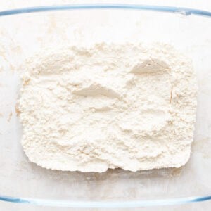 Flour in a glass bowl on a white surface.