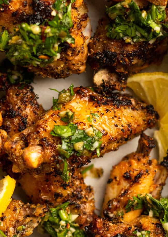 close up of lemon pepper wings with gremolata and lemon wedges.
