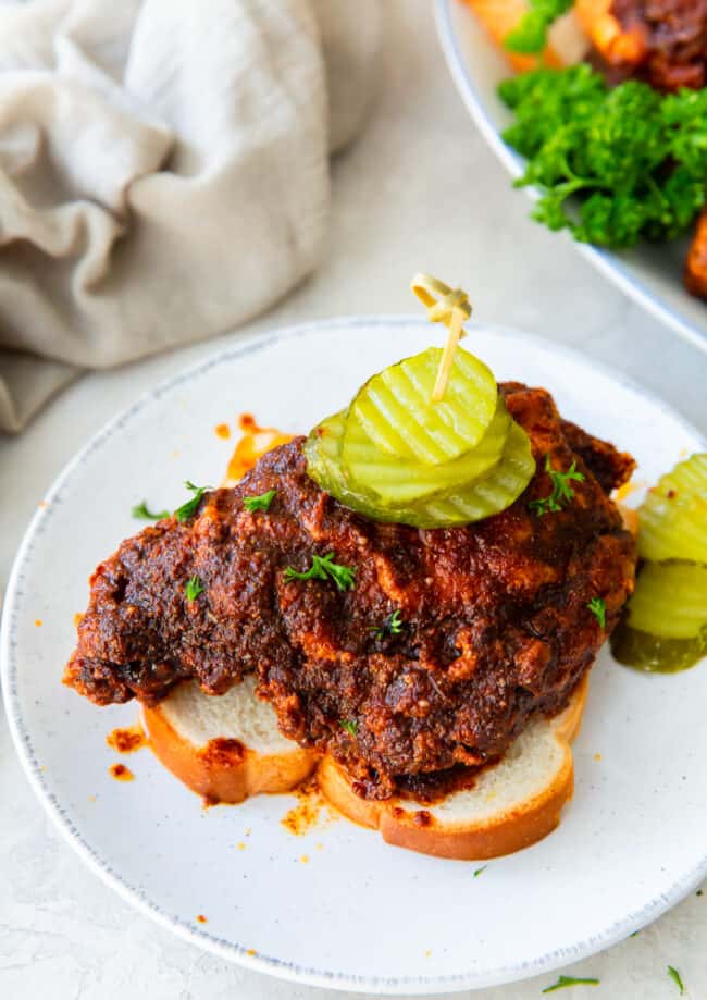 piece of nashville hot chicken on a slice of white bread topped with pickles